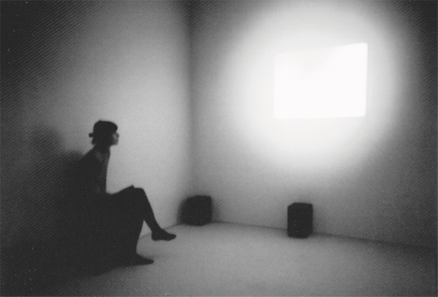 Installation view of "Atmos" by Gibson + Recoder, woman sitting in front of bright area of projected light