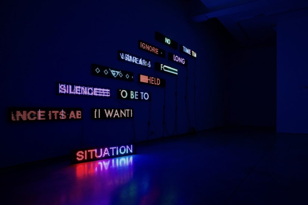 LED signs of different colors with words hung on a dark wall